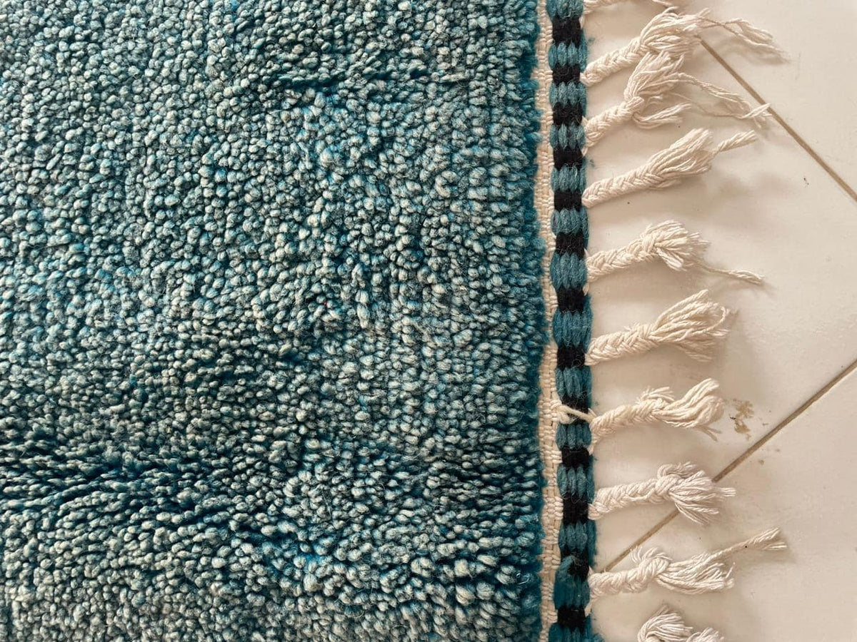 Close-up detail of the blue edge of a Moroccan rug with fringe detail and textured surface.