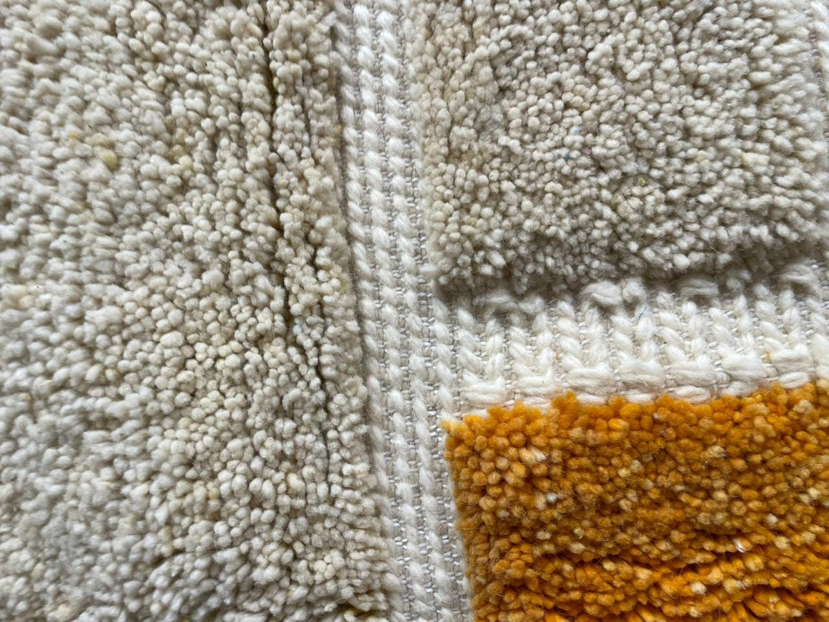 Close-up of a textured Moroccan rug displaying soft fibers in gray and orange.