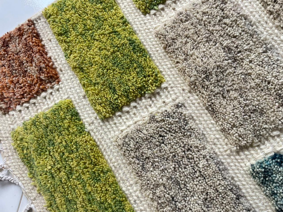 Detail shot of the textured patterns on a colorful Moroccan rug with green, gray, and orange tones.