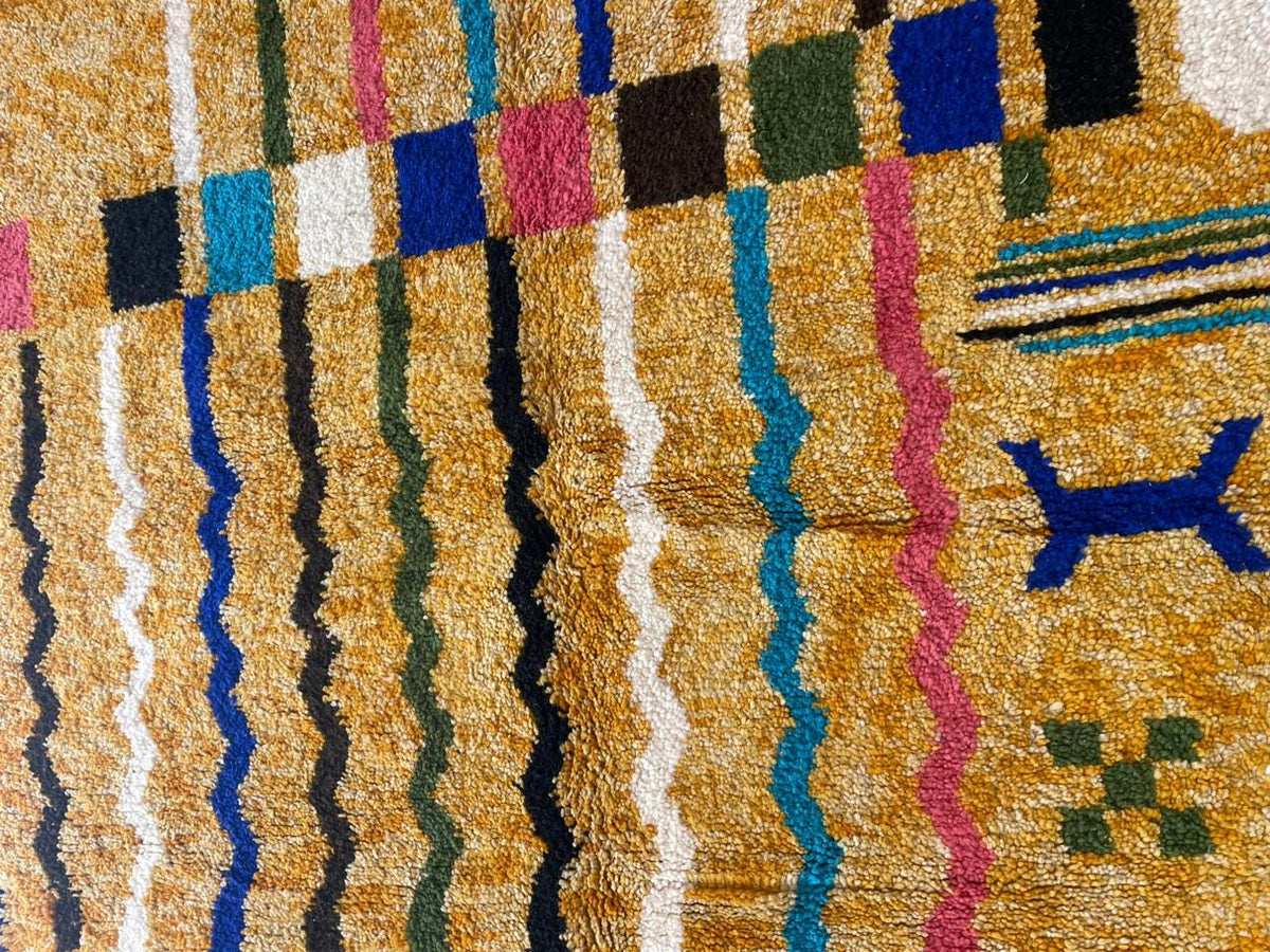 Detail close-up of a colorful Moroccan rug highlighting geometric patterns in yellow, blue, pink, and black.