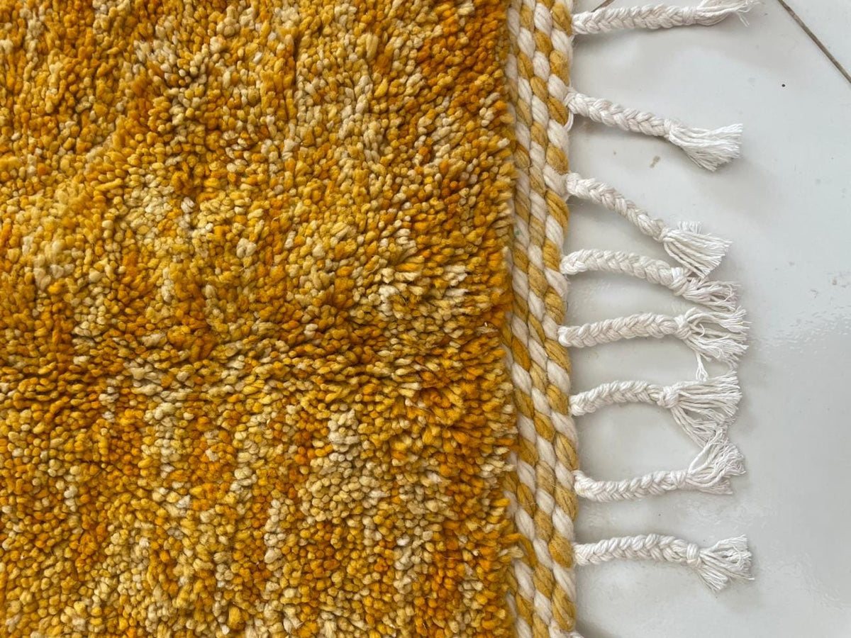 Detail close-up of a yellow textured rug with fringe edges.