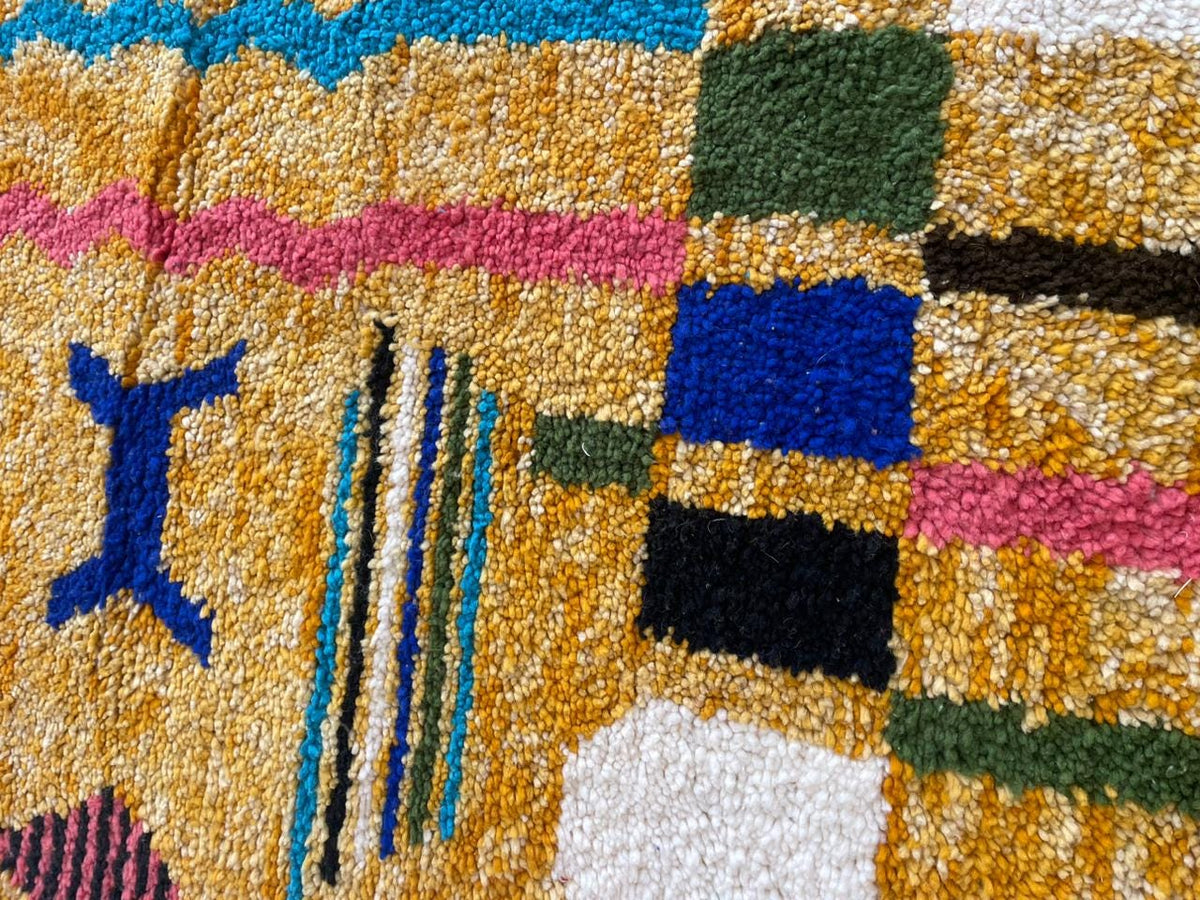 Detail close-up of a colorful Moroccan rug with geometric patterns in yellow, blue, pink, and black.