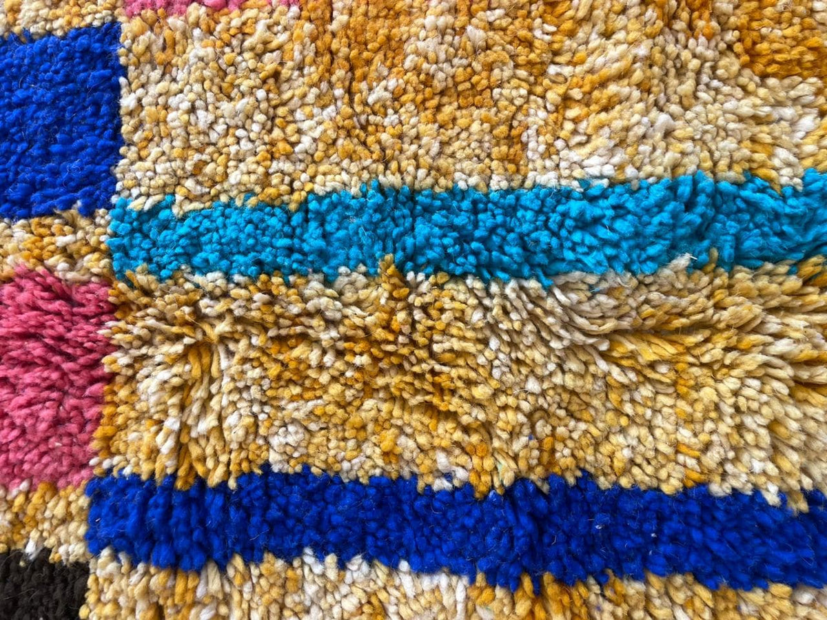 Detail close-up of a colorful Moroccan rug showcasing a striped pattern in yellow, blue, green, and pink.