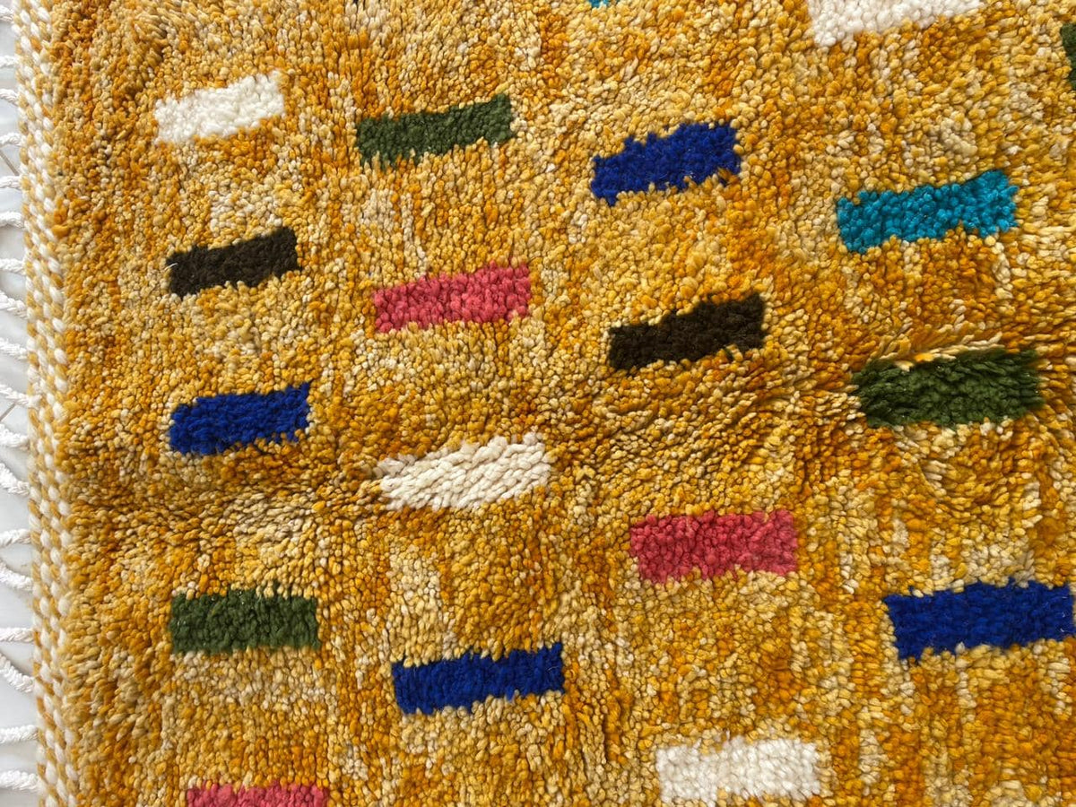 Detail close-up of a colorful Moroccan rug with a block pattern in yellow, blue, green, and pink.