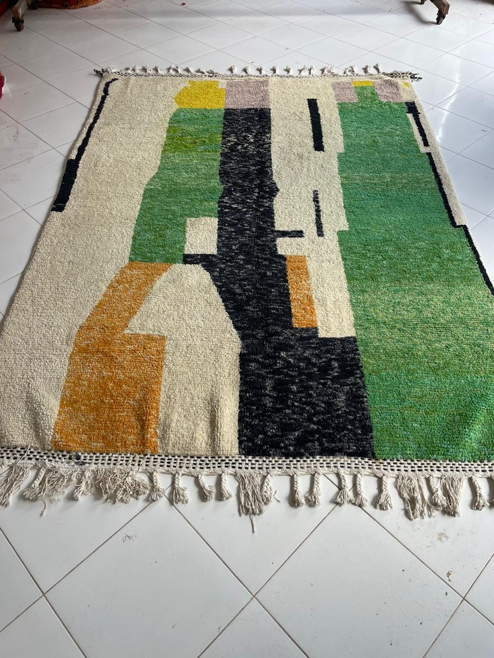 Lifestyle shot of a colorful rug with geometric design and fringed edges in a natural setting.