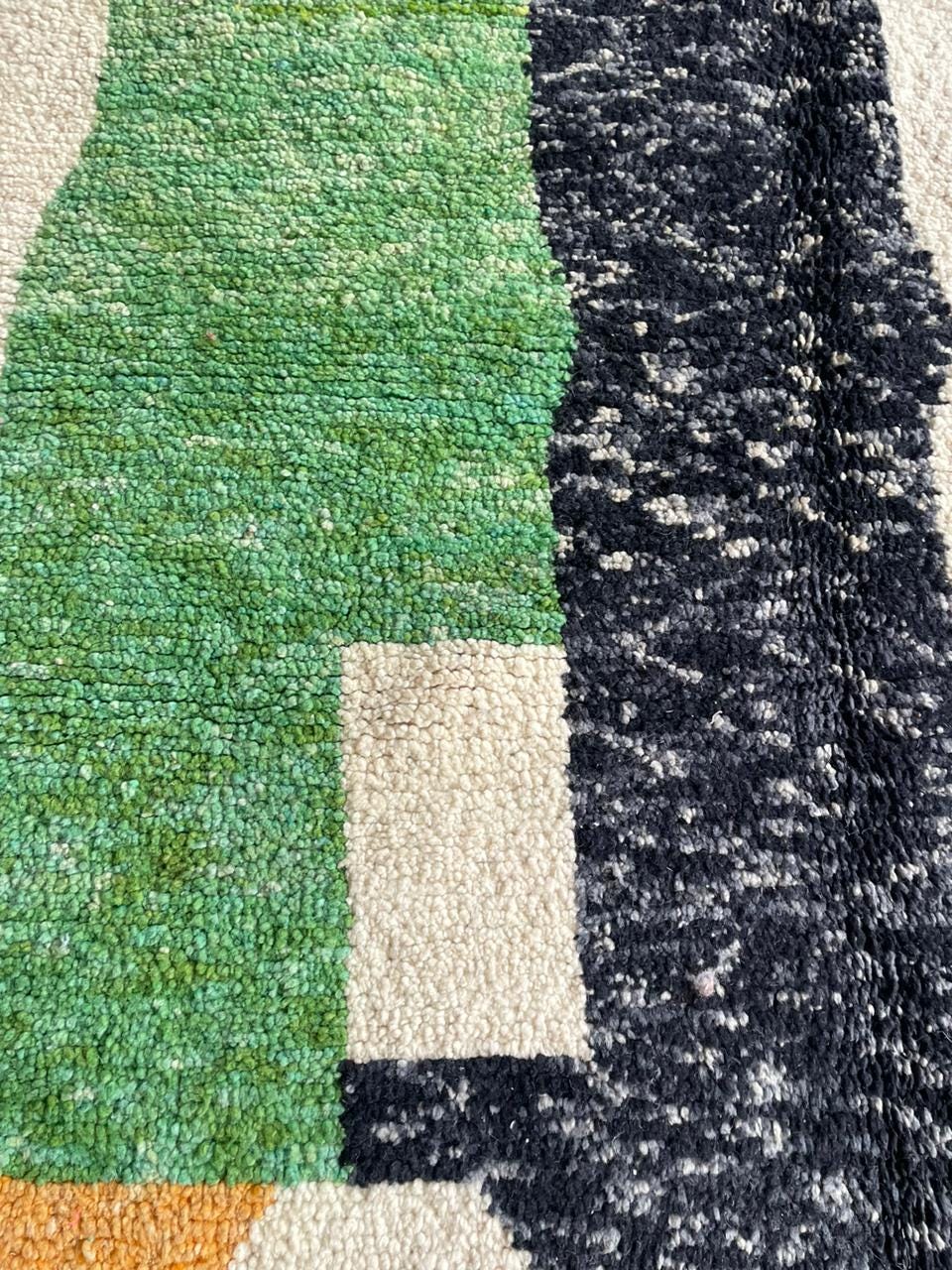 Close-up detail of a textured rug showing colorful sections in green, black, and cream.