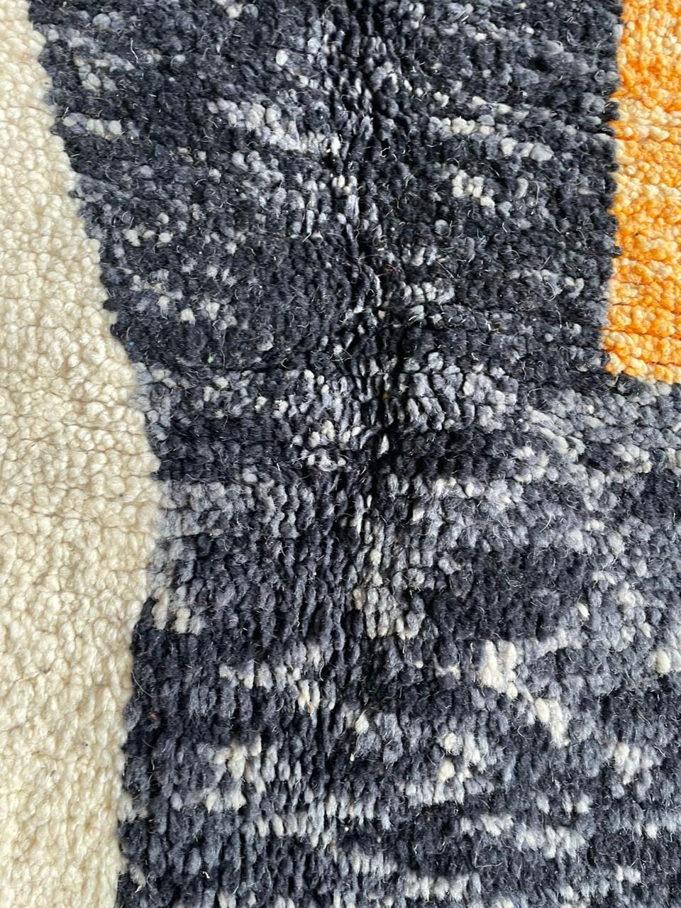 Close-up detail of a textured rug featuring an abstract pattern in navy, cream, and orange.