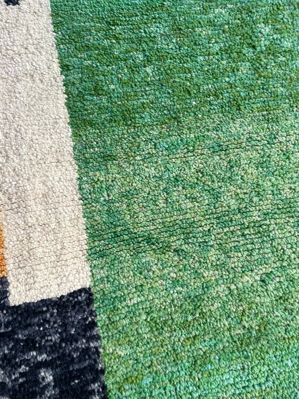 Close-up detail of a textured rug featuring colorful sections in green, black, and cream.