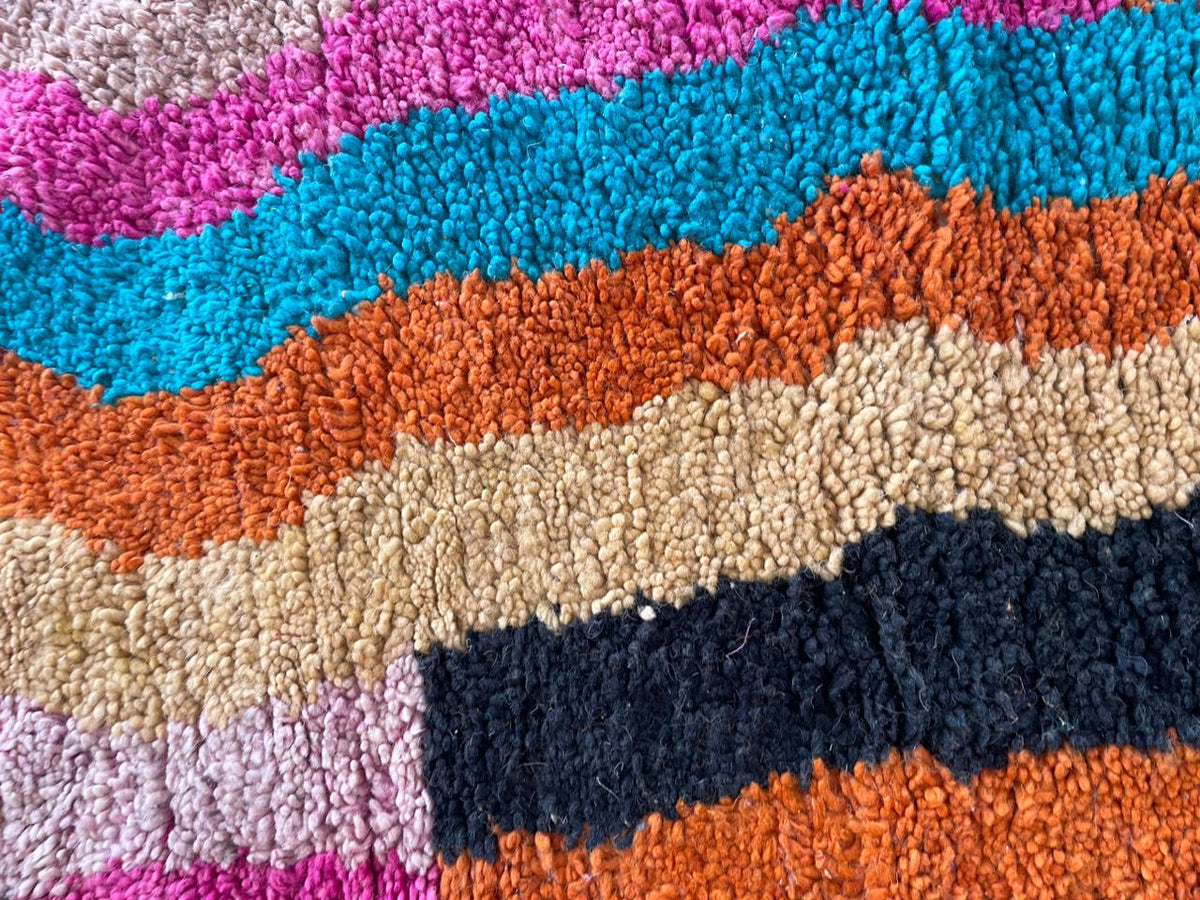 Close-up detail of a textured surface on a colorful Moroccan rug with a striped pattern in blue, orange, and cream.