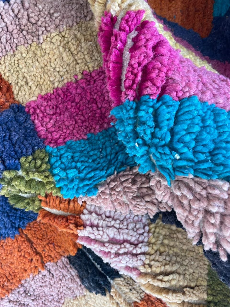 Detail shot of a colorful woven rug with a multicolored pattern in pink, blue, green, and purple.