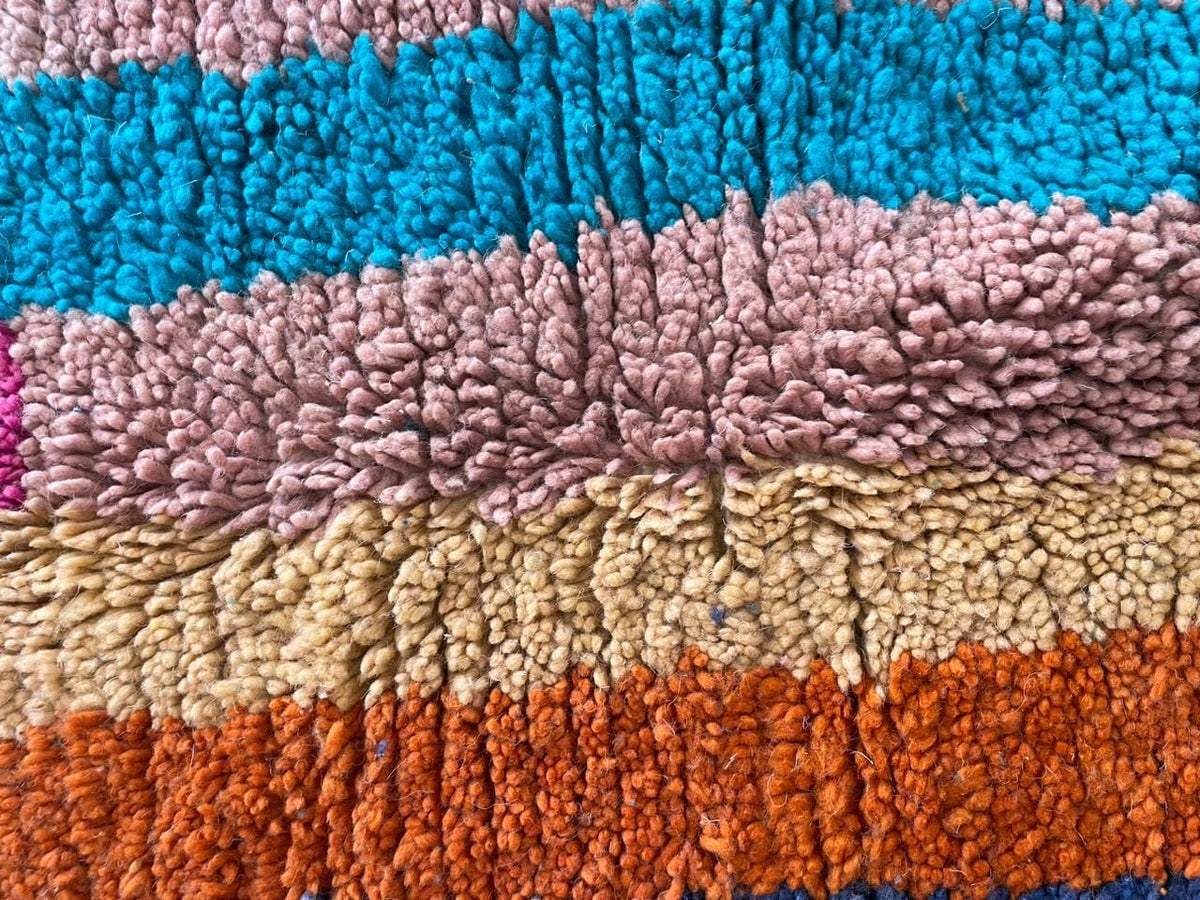 Detail shot of a colorful Moroccan rug showcasing a striped pattern in pink, yellow, blue, and orange.