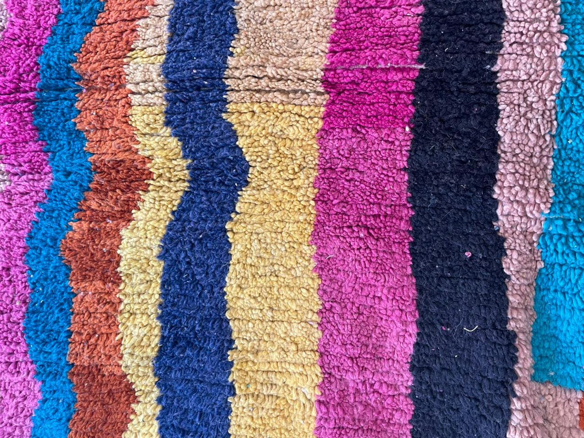 Detail shot of a colorful Moroccan rug featuring a striped pattern in pink, yellow, blue, and orange.