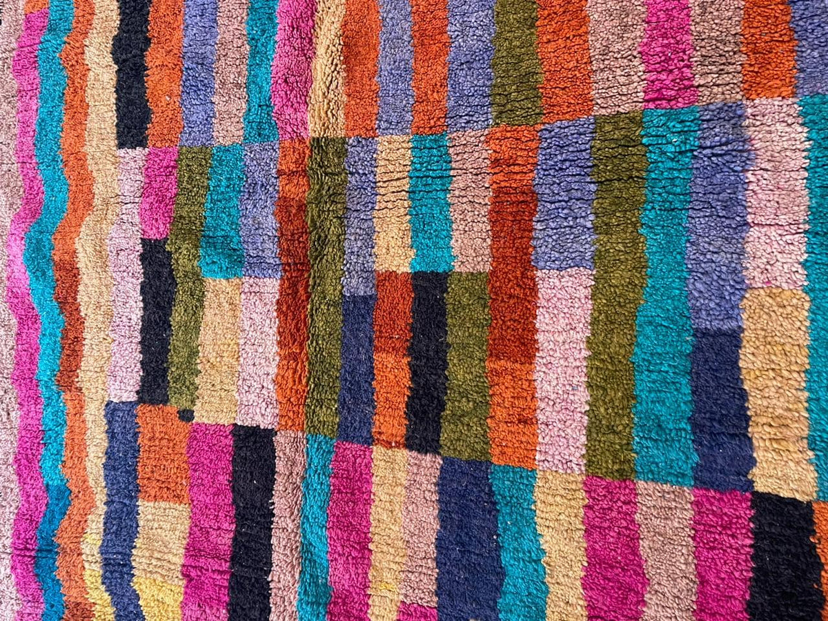 Top view of a colorful Moroccan rug showcasing a striped pattern and fringed edges in pink, blue, and brown.