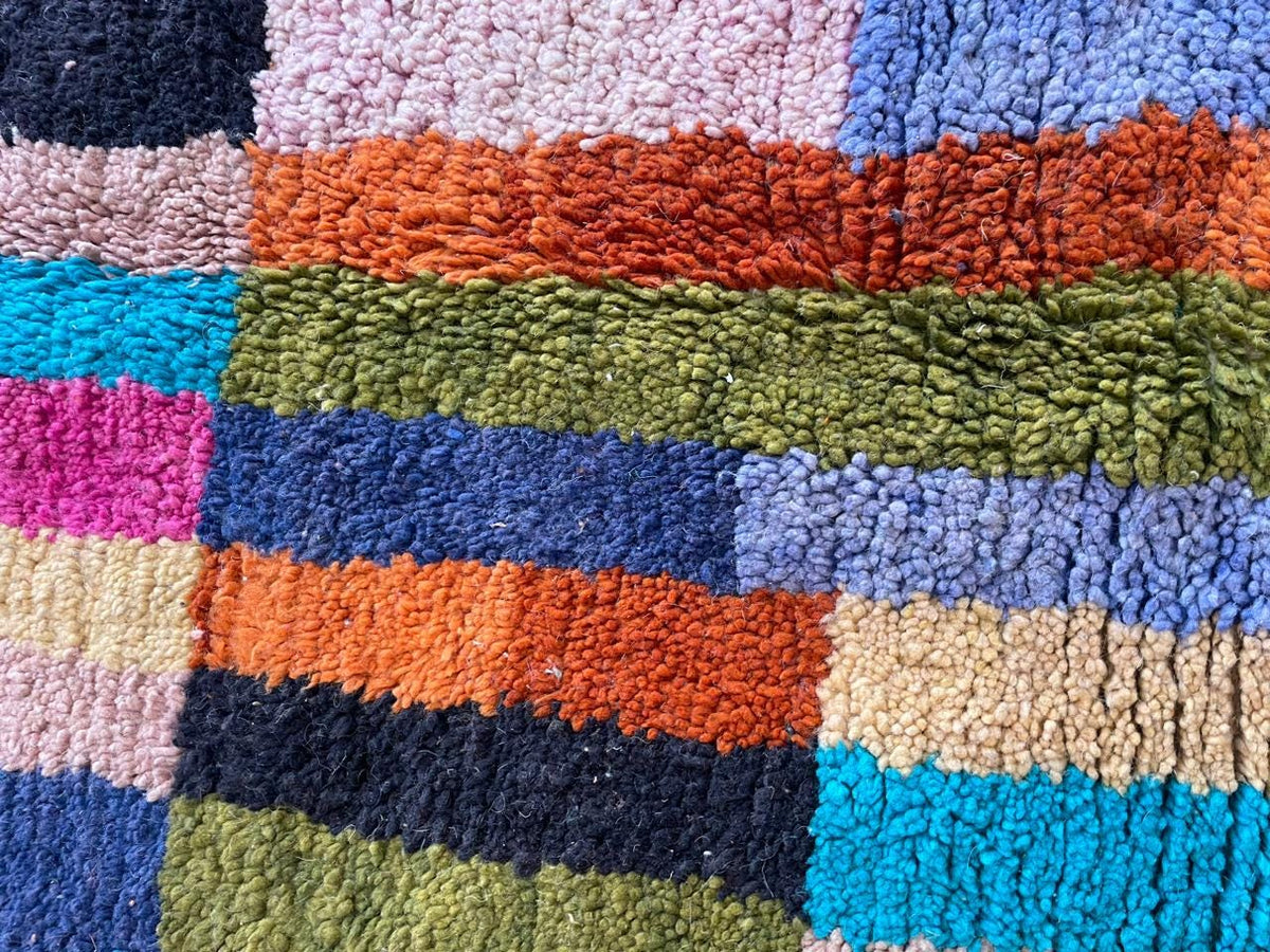 Detail shot of a colorful Moroccan rug with a striped pattern in pink, orange, green, and blue.