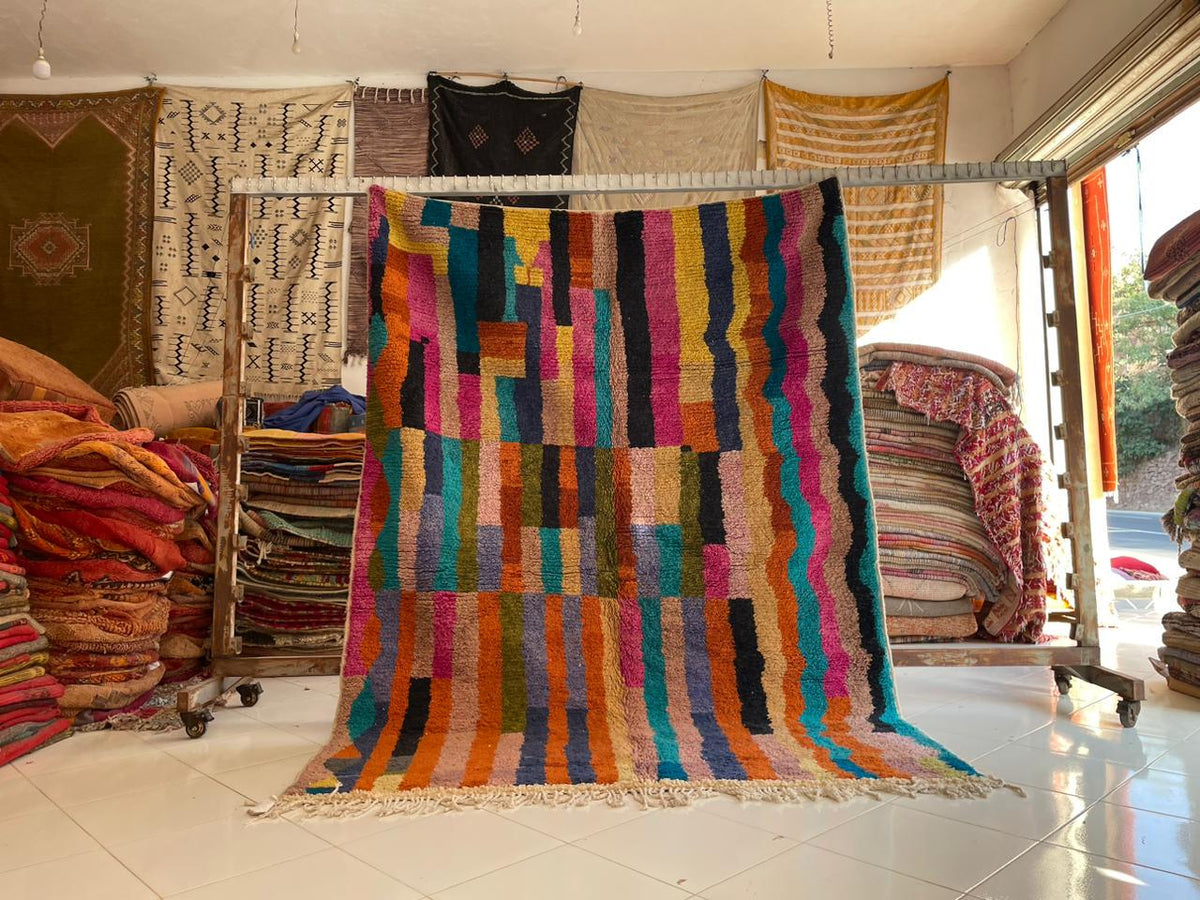 Lifestyle shot of a striped Moroccan rug display in orange, blue, green, and yellow.