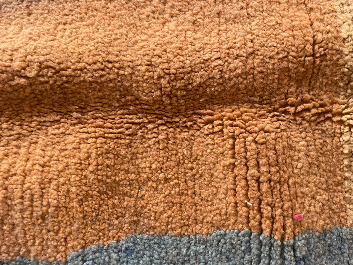 Close-up detail of a colorful Moroccan rug featuring smooth surface with abstract shapes in orange, blue, and brown.