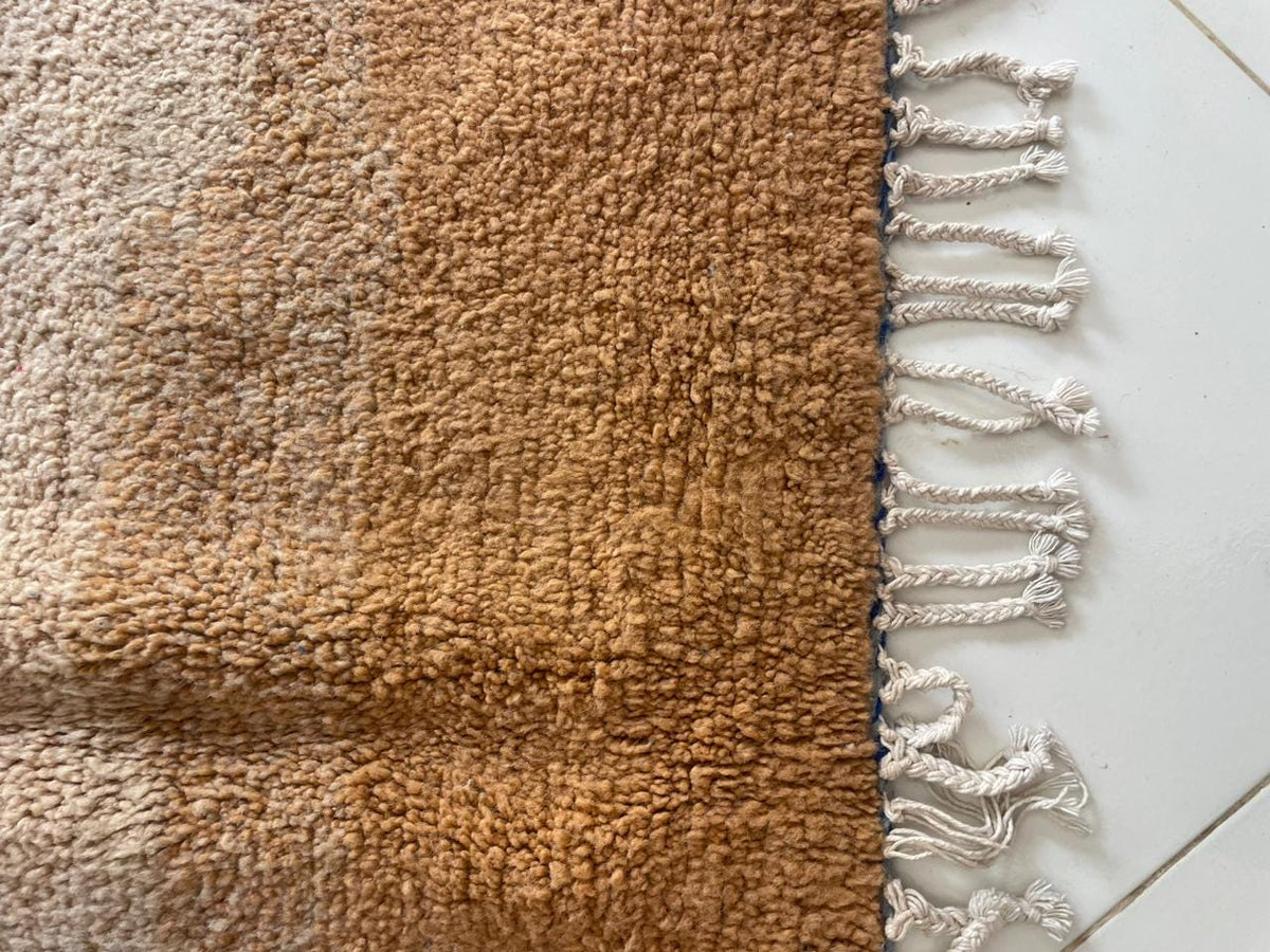 Close-up detail of a brown textured rug with fringe edges and a soft texture in brown and beige.