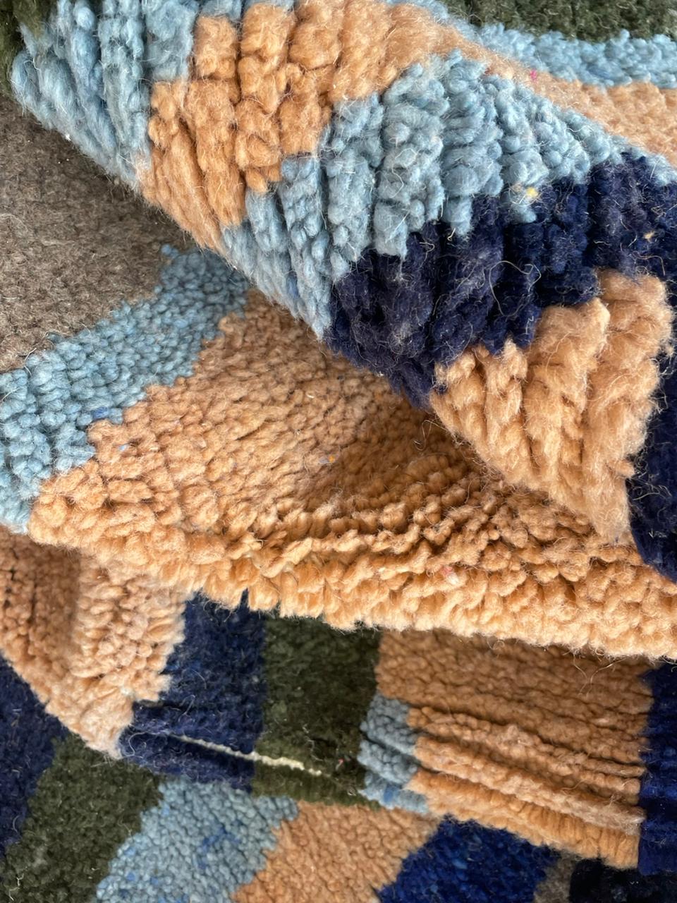 Close-up detail of a colorful Moroccan rug with folded edges and textured fabric in orange, blue, and green.