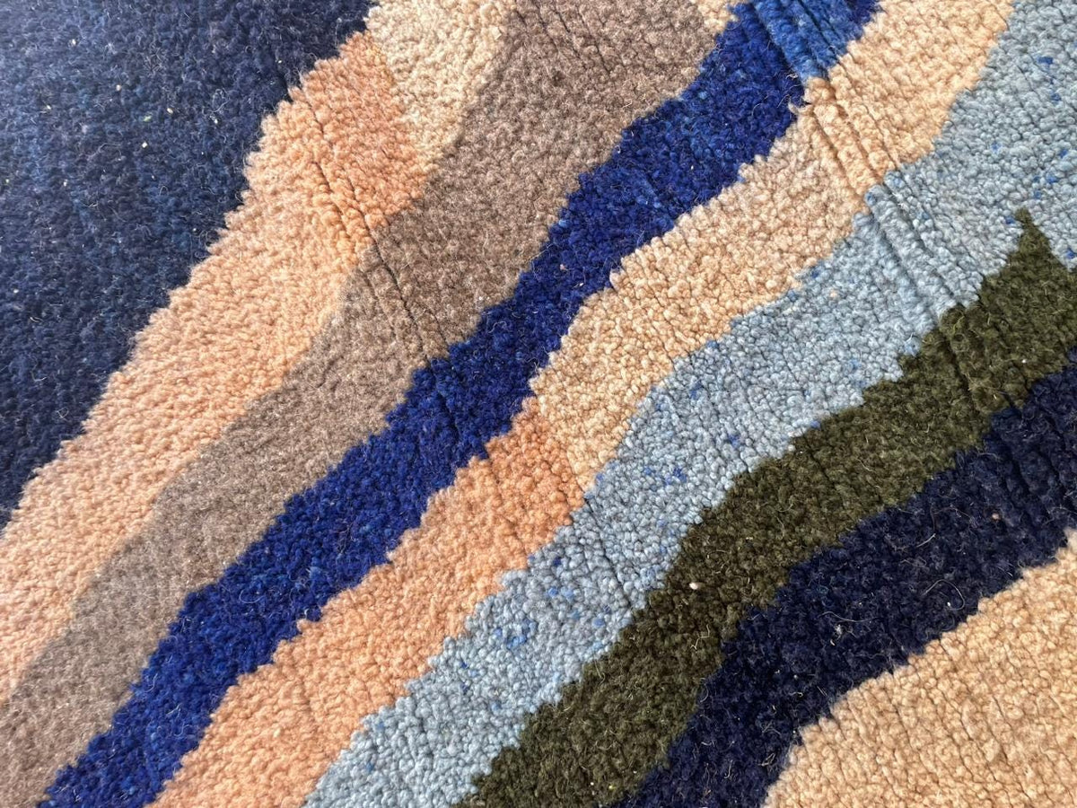 Close-up detail of a colorful Moroccan rug displaying a striped design in beige, blue, brown, and green.