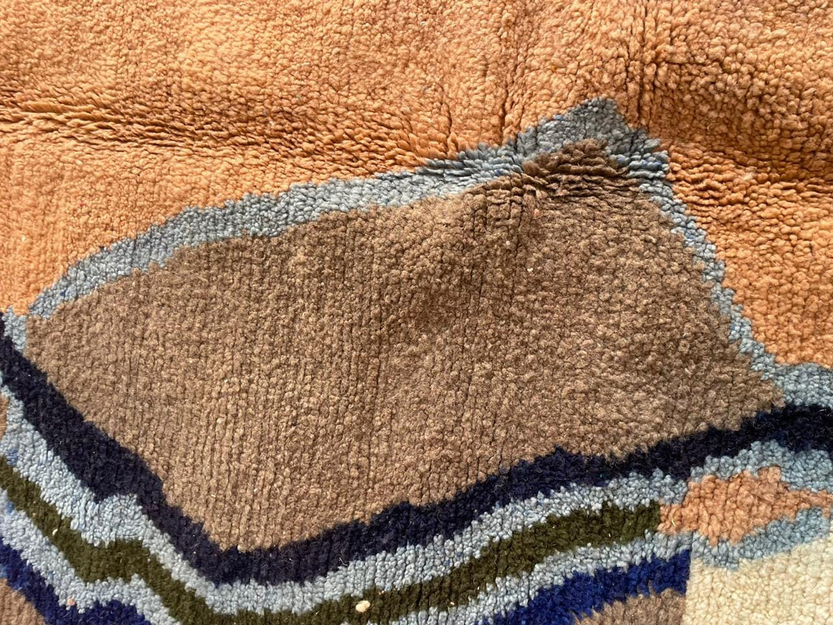 Close-up detail of a colorful Moroccan rug with a soft texture and layered design in orange, brown, and blue.