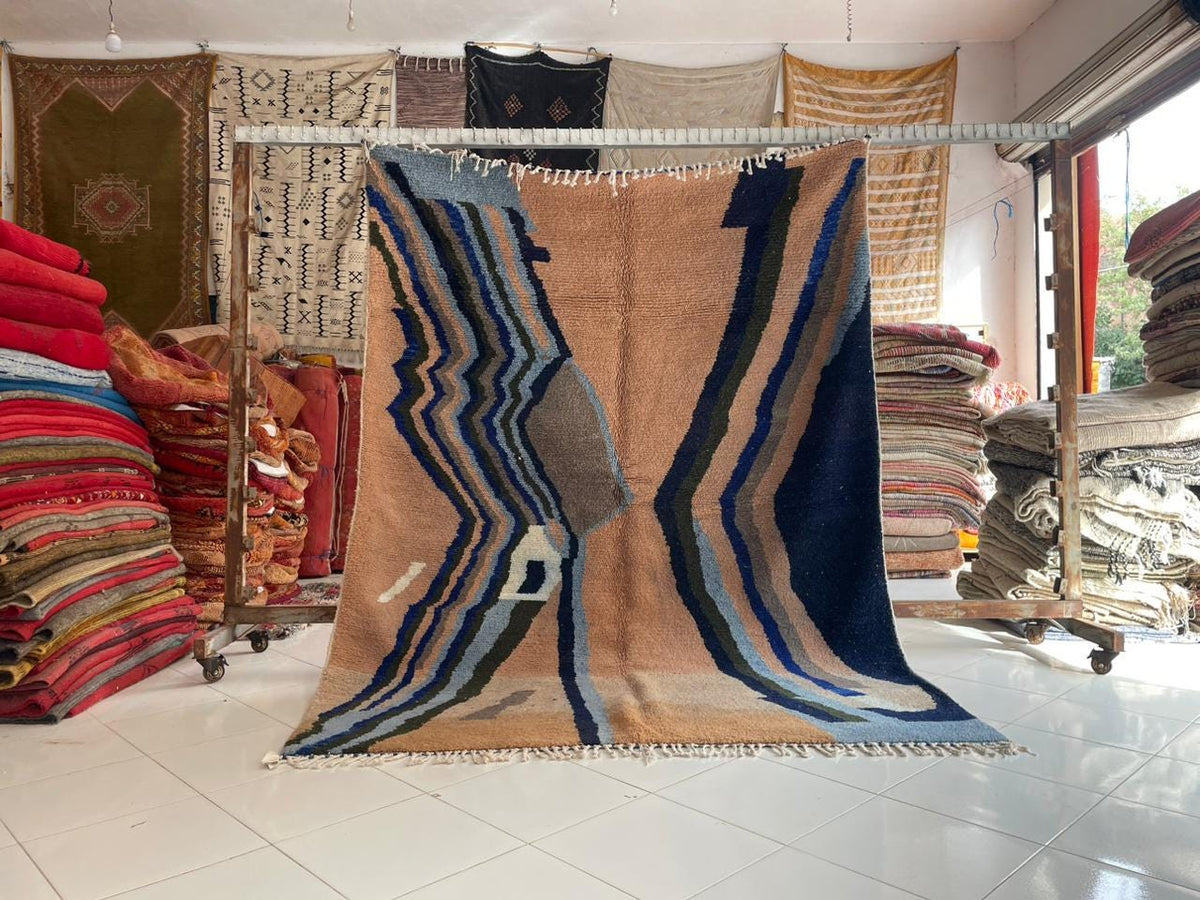 Lifestyle shot of a colorful Moroccan rug showcasing geometric patterns and large size in beige, blue, and brown.