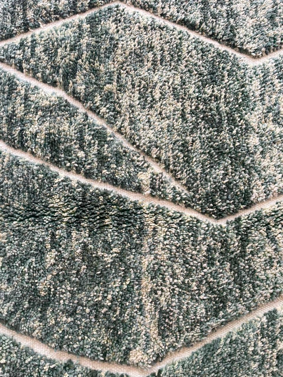 Close-up detail of textured fibers and a straight line pattern on a green Moroccan rug.