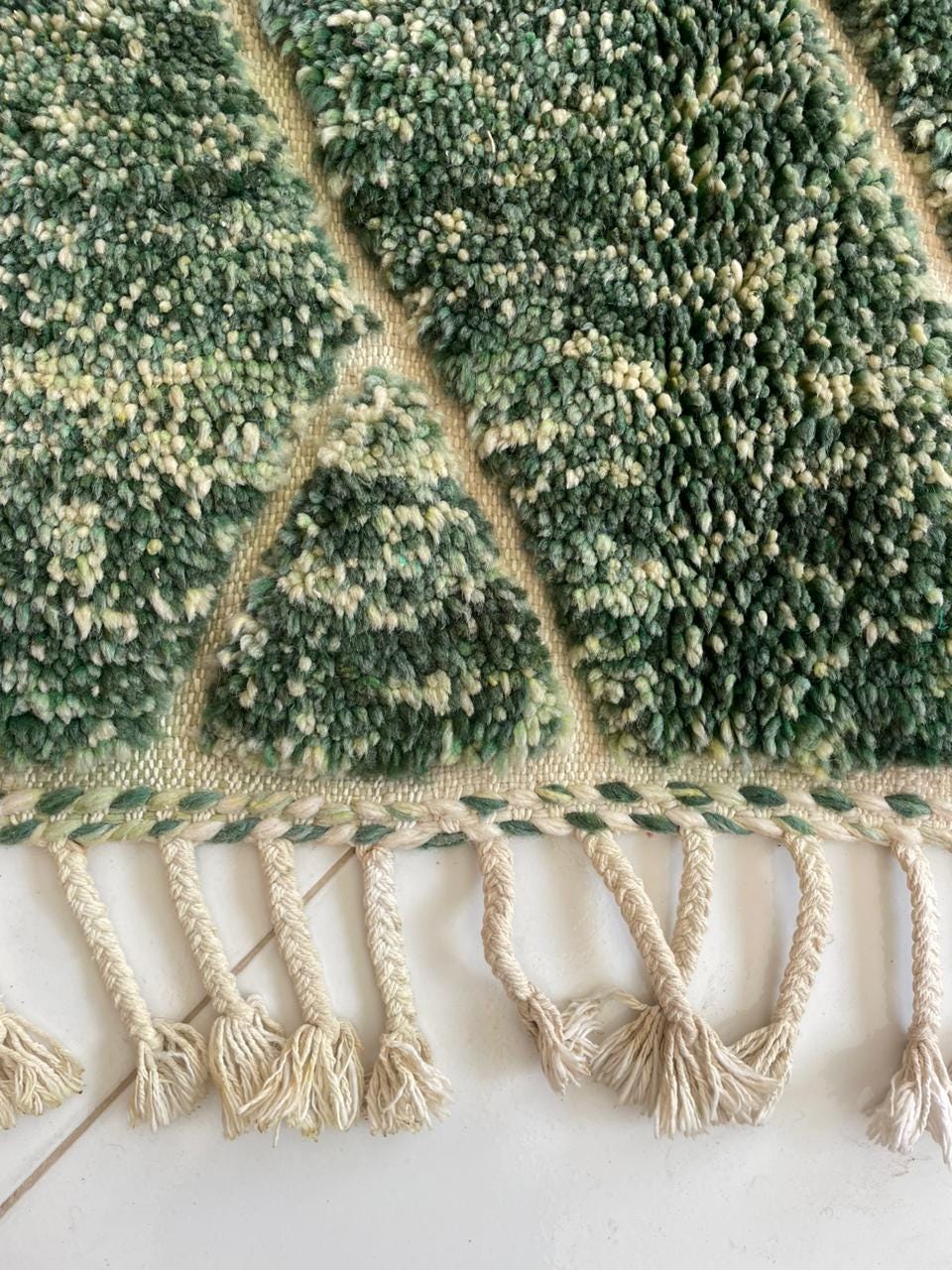 Close-up detail of a green patterned rug with fringed edges.
