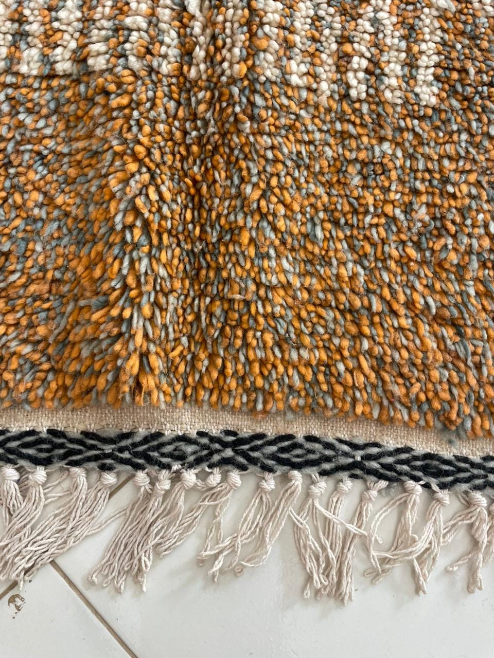 Close-up detail of fringe on orange, gray, and white Moroccan rug.