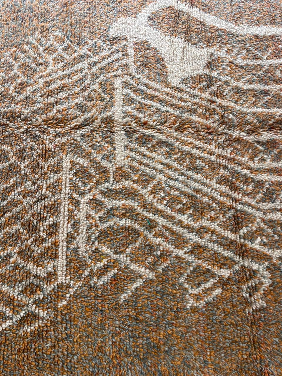 Close-up view of orange, gray, and white Moroccan rug with geometric pattern.