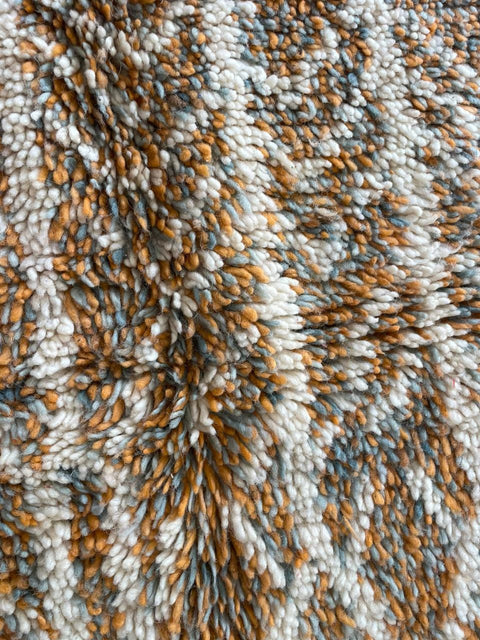 Close-up detail of textured pattern on orange and gray Moroccan rug with soft fibers.