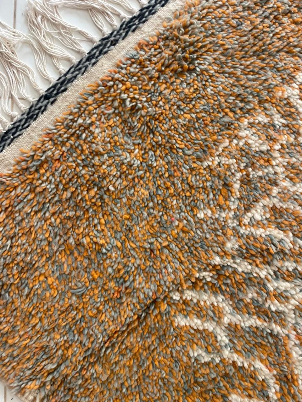 Close-up detail of textured surface on orange, gray, and white Moroccan rug.