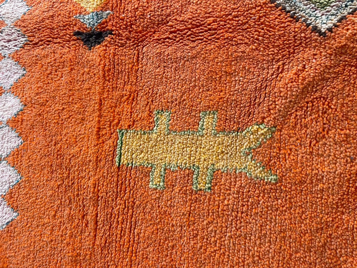 Close-up detail of an orange Moroccan rug featuring decorative stitching.