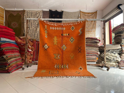 Lifestyle shot of an orange rug with decorative patterns on a natural background.