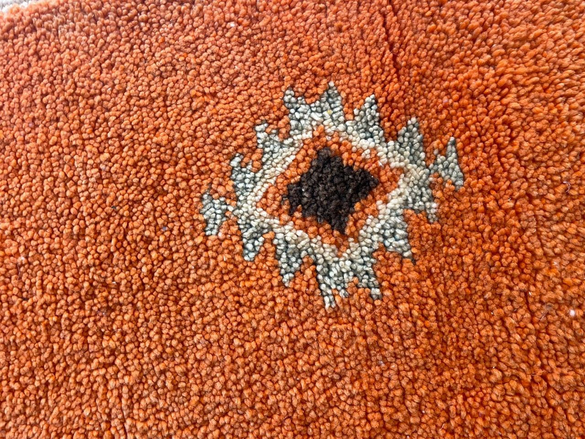 Close-up detail of an orange Moroccan rug displaying a geometric pattern.