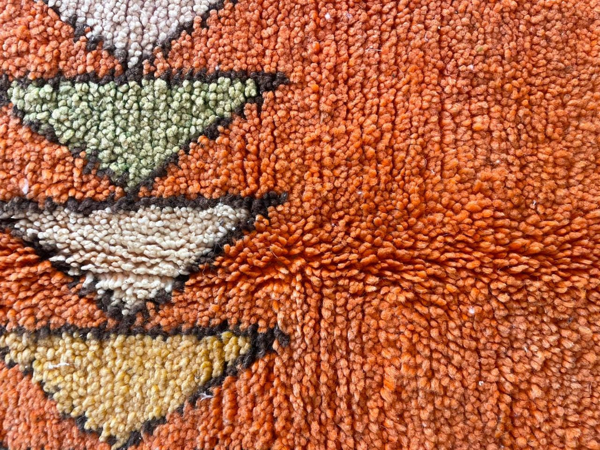 Close-up detail of an orange Moroccan rug with triangular patterns and woven texture.