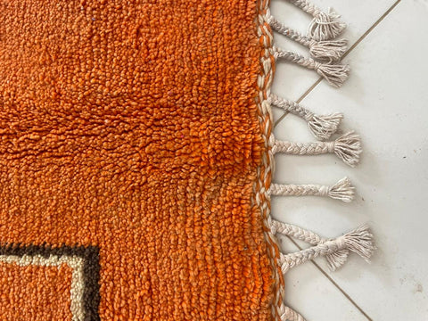 Close-up detail of an orange Moroccan rug highlighting fringe detail.