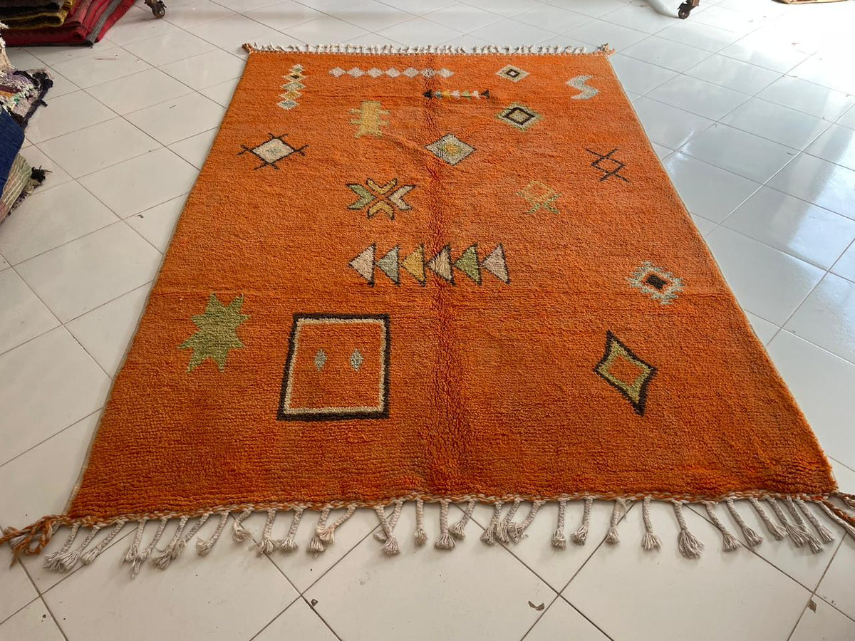 Front view of an orange Moroccan rug featuring decorative motifs and fringed edges against a white background.