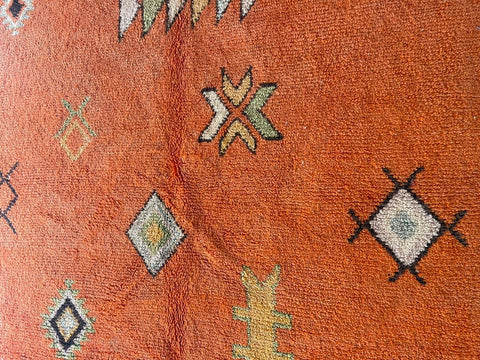 Close-up detail of an orange Moroccan rug showcasing intricate designs and textured fabric.