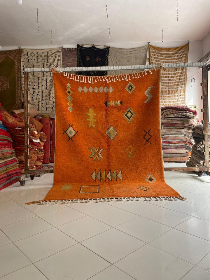 Lifestyle shot of an orange Moroccan rug with geometric patterns on a natural background.