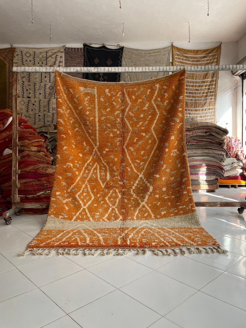 Lifestyle shot of an orange Moroccan rug with fringe edges on a natural background.