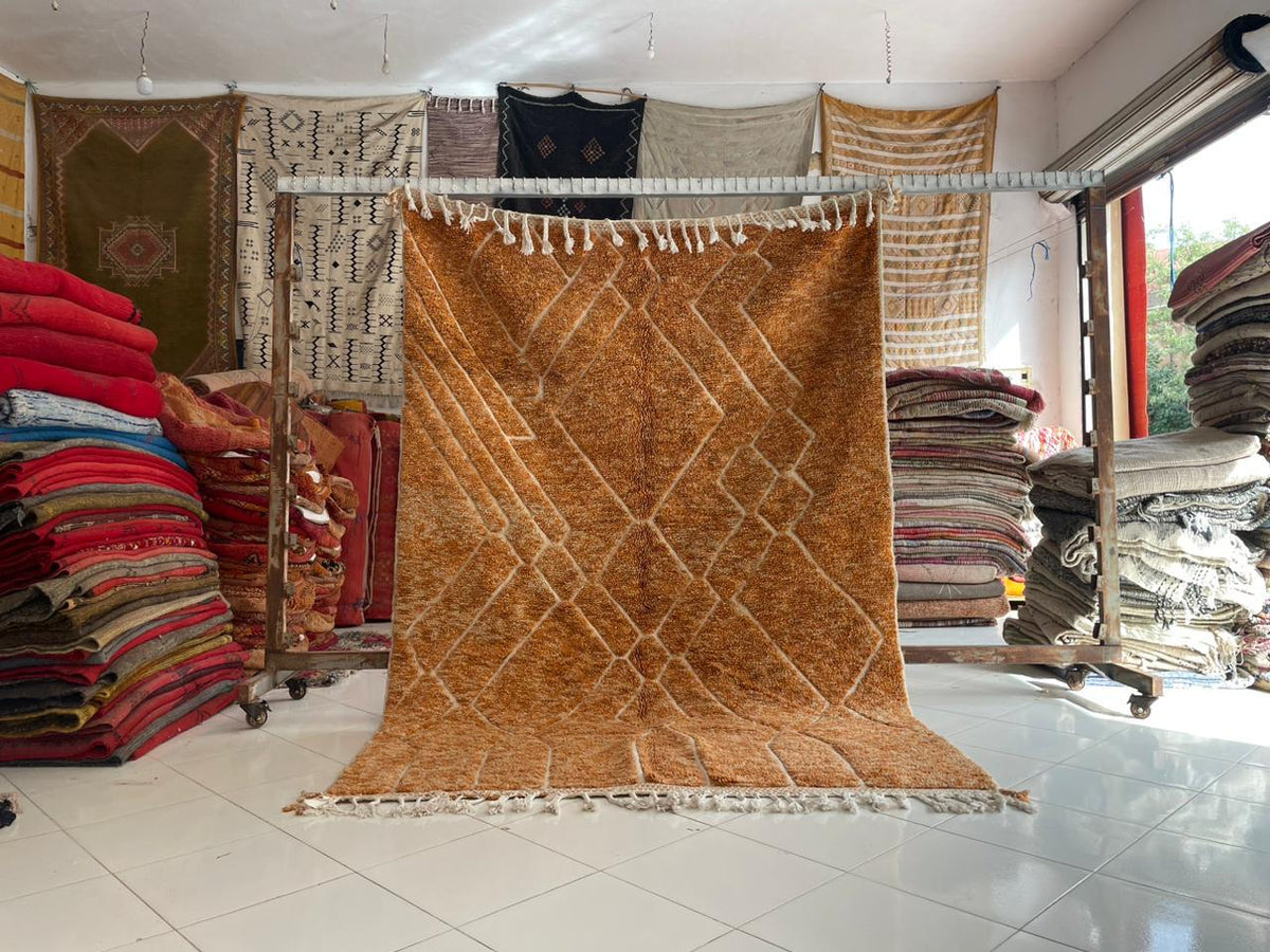 Lifestyle display of an orange Moroccan rug with various rugs in the background.