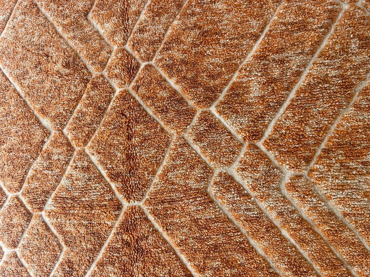 Close-up detail of an orange Moroccan rug showcasing a geometric design and soft texture.