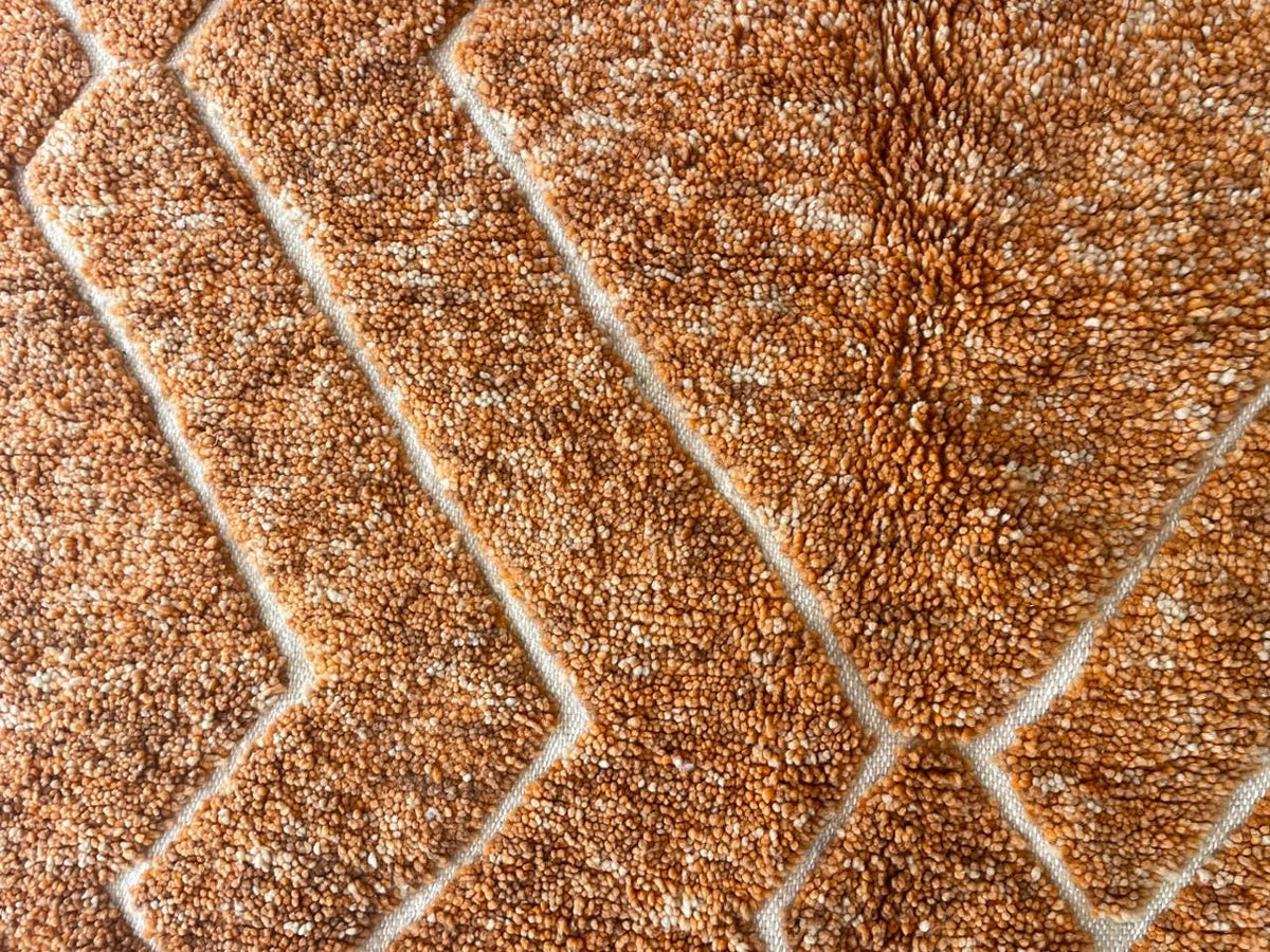 Detail view of an orange Moroccan rug featuring a textured surface.