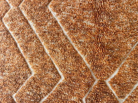 Detail view of an orange Moroccan rug featuring a textured surface.