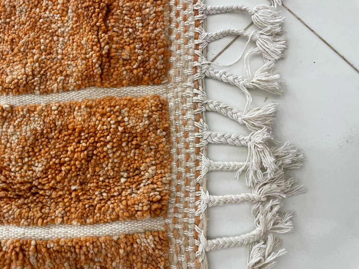 Detail shot of an orange Moroccan rug with a fringed edge.