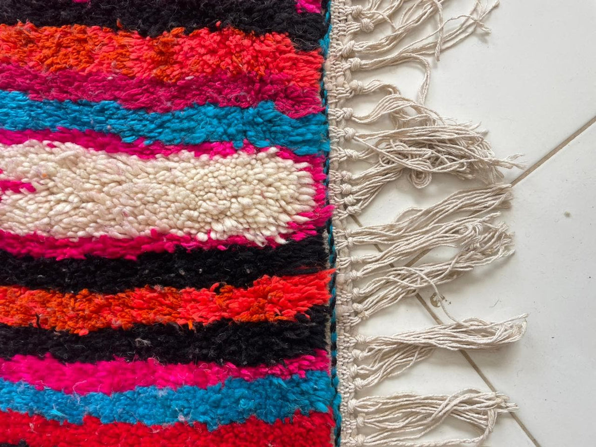 Close-up detail of a colorful pink rug with a striped pattern and fringe edges.