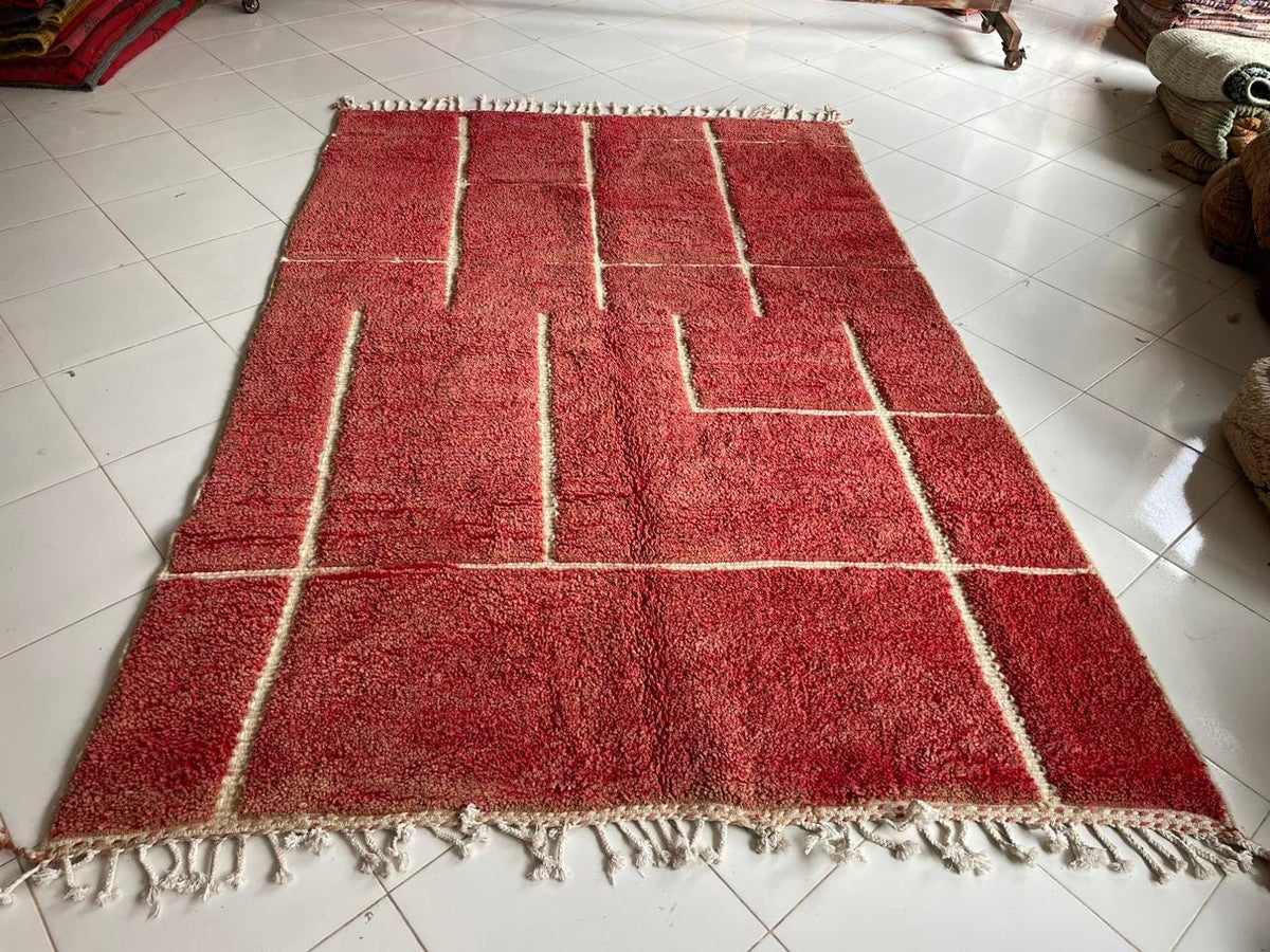 Top view of a red Moroccan rug featuring fringe edges against a natural background.