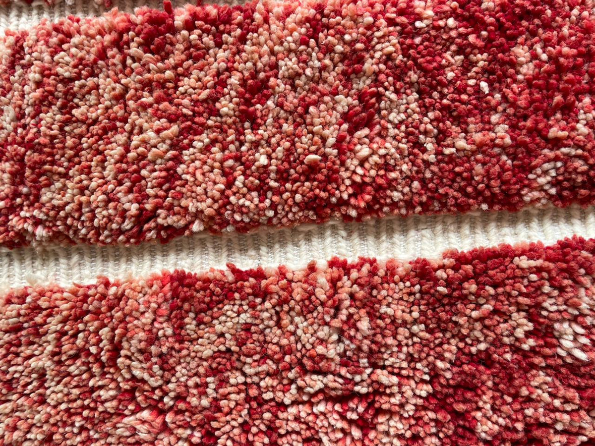 Close-up texture view of a red Moroccan rug on a white background.