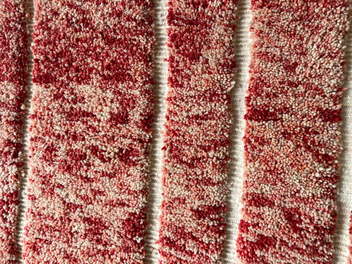 Close-up detail of the textured surface of a red Moroccan rug on a white background.