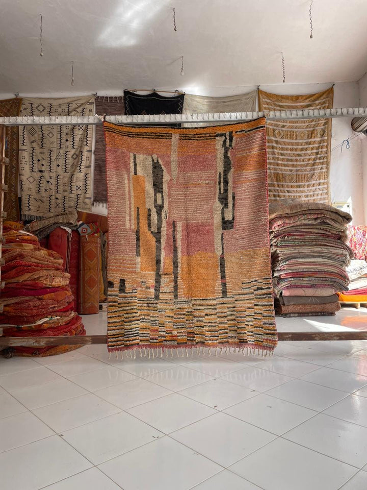Lifestyle shot of a colorful Moroccan rug with tribal patterns in orange, red, and black.
